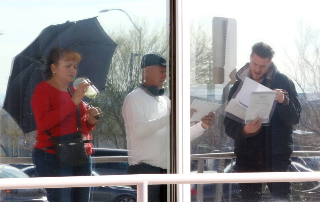 People are reflected on glass windows as they wait in line at One-Stop Career Center on Monday, ...