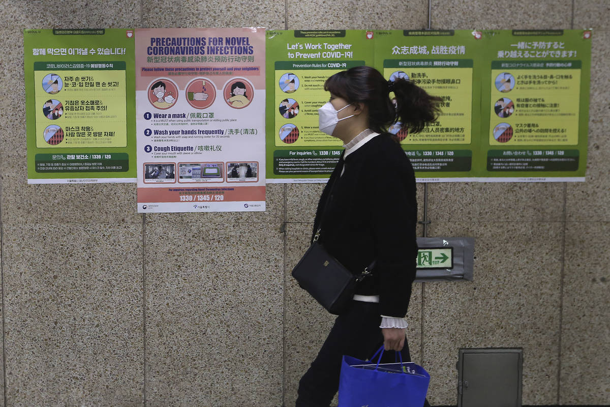A woman wearing a face mask passes by posters about precautions against new coronavirus at a su ...