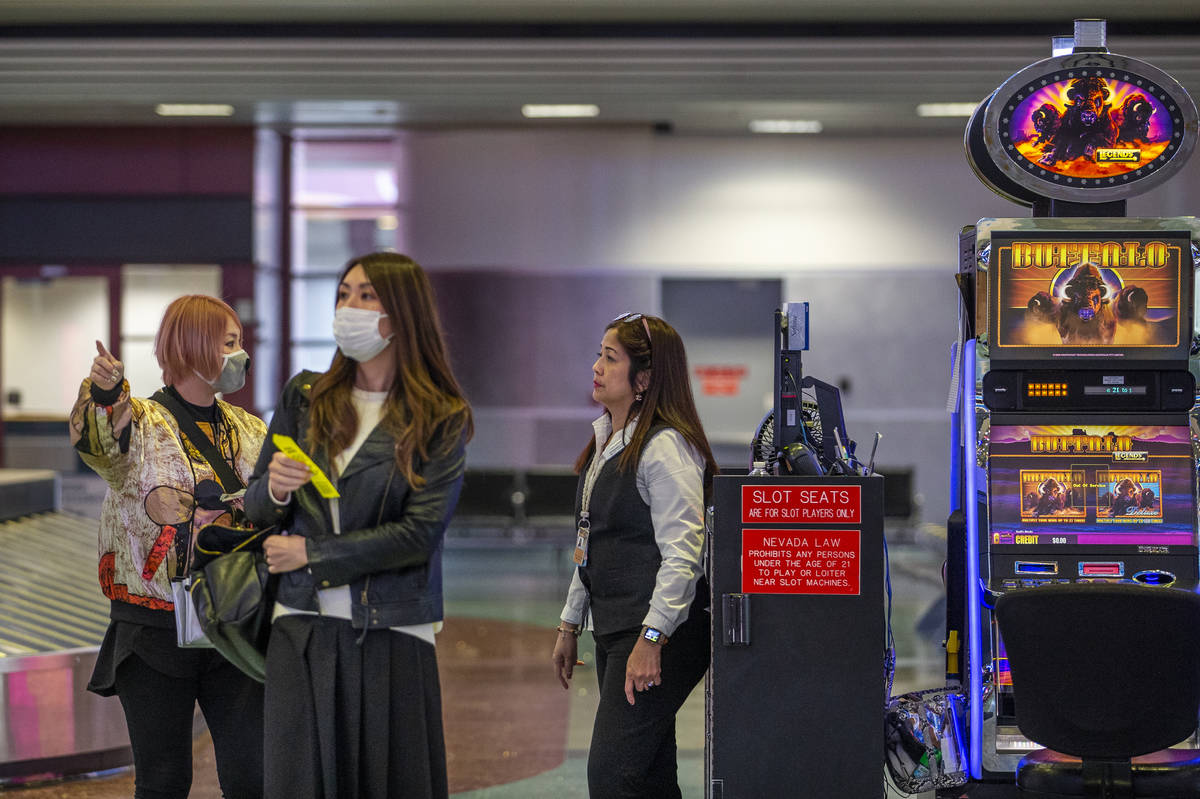 Masked passengers say for directions from slots employee Marites Mallari, right, in the baggage ...