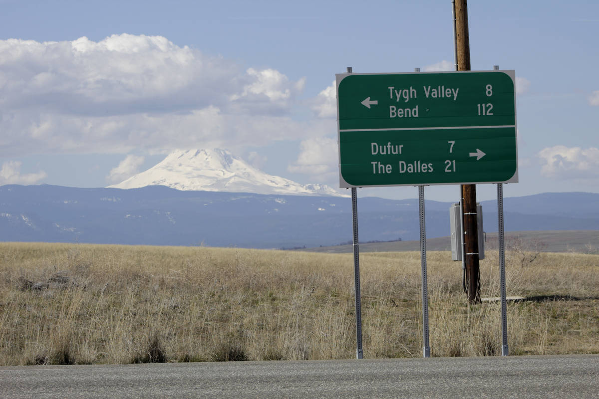 A sign indicates the distance to the nearest towns as cloud-capped Mount Hood rises in the back ...