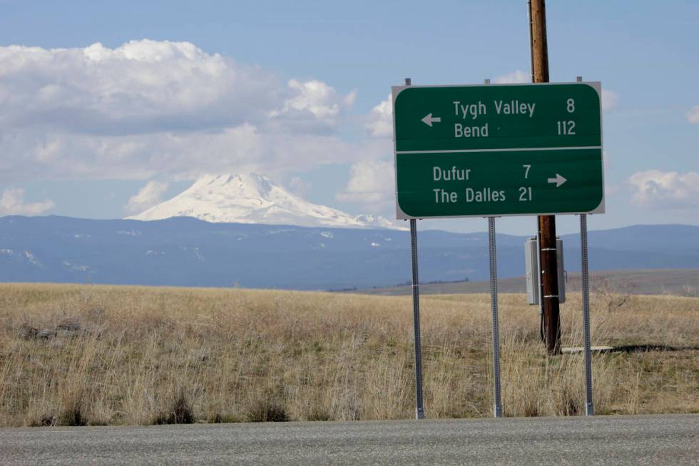 A sign indicates the distance to the nearest towns as cloud-capped Mount Hood rises in the back ...