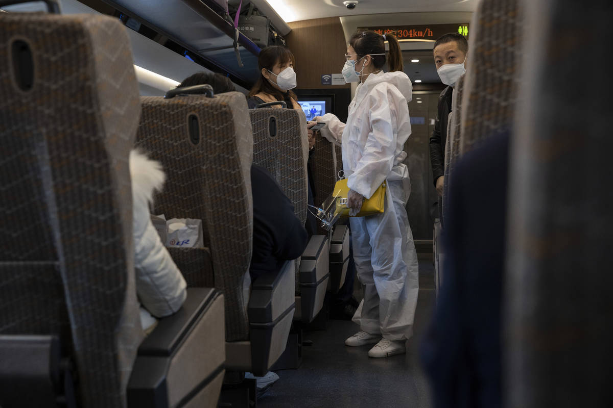 A traveler wearing a protective suit chats with another onboard a train leaving from the train ...