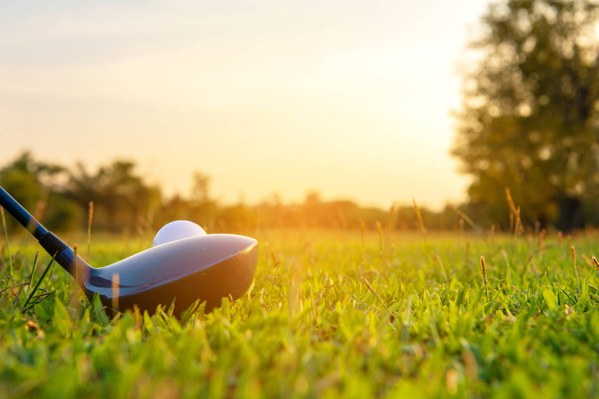 Close up golf ball and driver, player doing golf swing tee off on the green sunset evening time ...