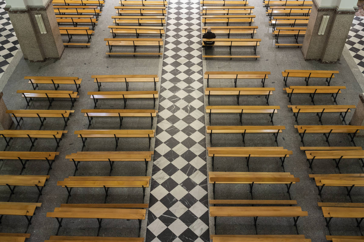 A Catholic priest sits on an empty bench due to social distancing guidelines during the coronav ...