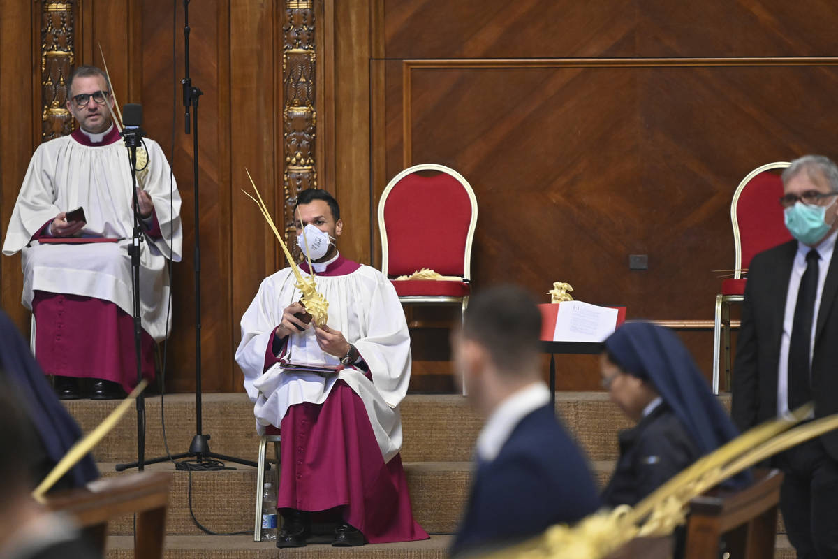 A prelate wearing a face mask holds a palm branch as waits for the start of the Pope's Palm Sun ...