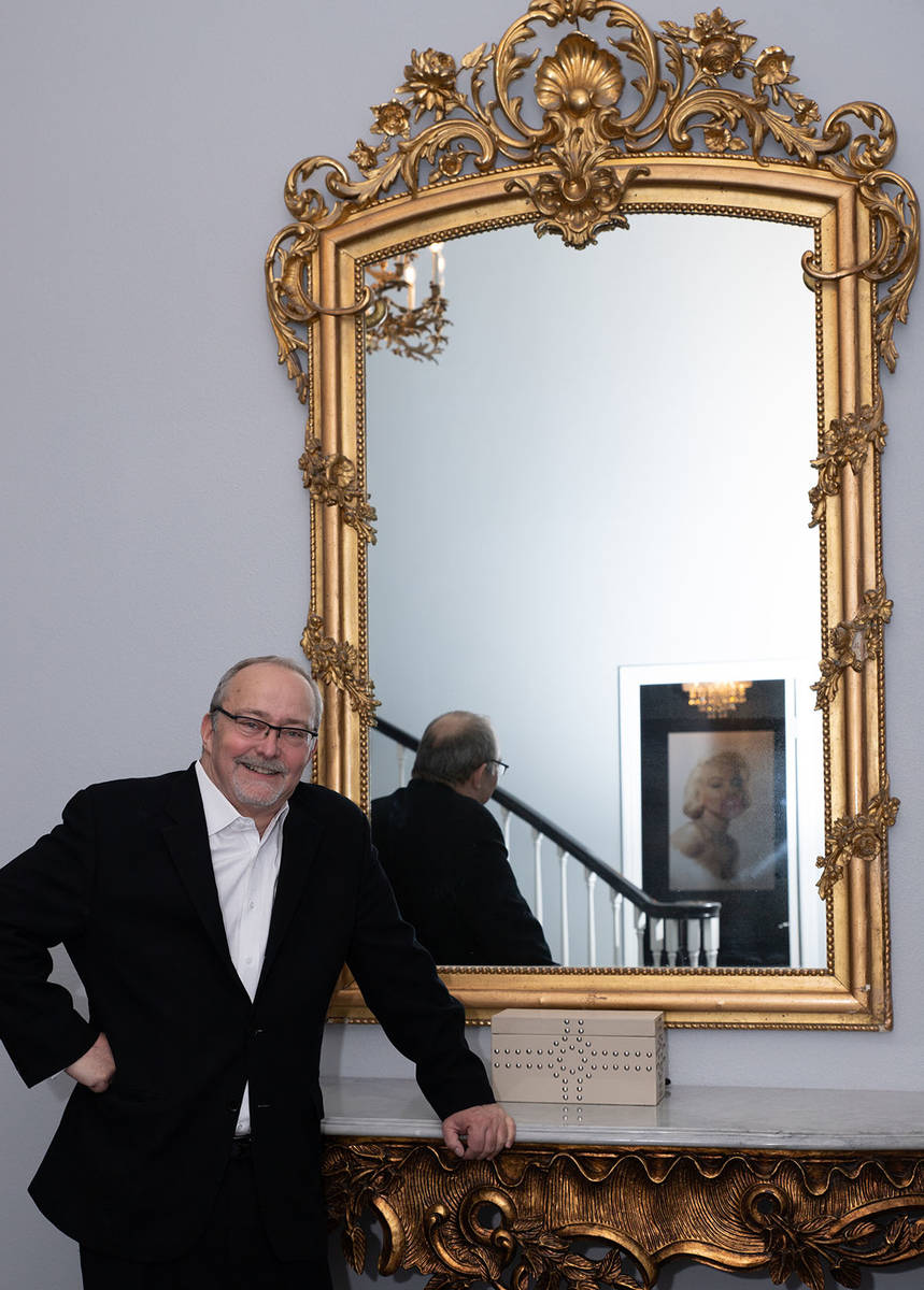 Myron Martin leans against an ornate entry table topped with a gilt-framed mirror, some of the ...