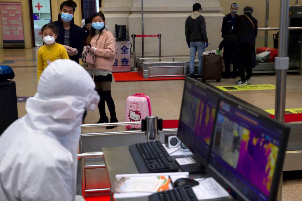 Passengers wearing face masks to protect against the spread of new coronavirus watch as a worke ...
