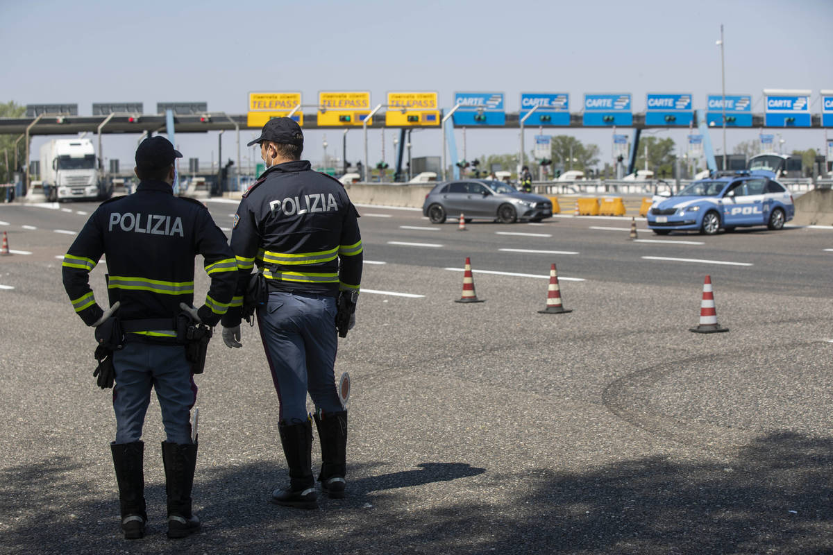 Police officers stop cars at the Melegnano highway barrier entrance, near Milan, Italy, Saturda ...