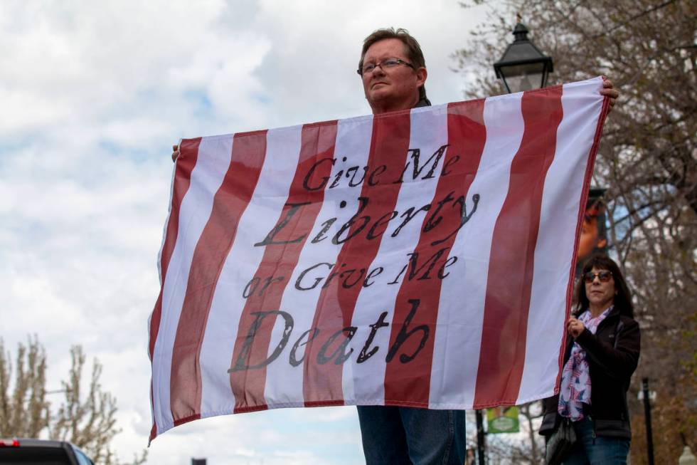 Brandon Camp, 50, holds a flag with the Patrick Henry quote "Give me liberty, or give me d ...