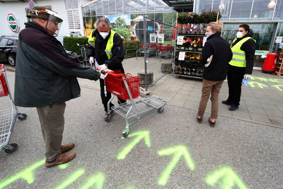 Security employee disinfect shopping carts at the entrance of a garden store in Munich, Germany ...