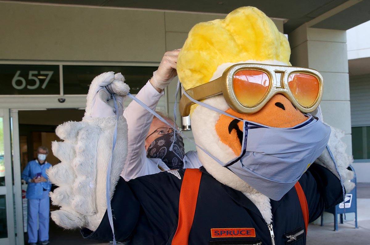 Las Vegas Aviators mascot Spruce dons a medical mask with the help of Director of Game Entertai ...