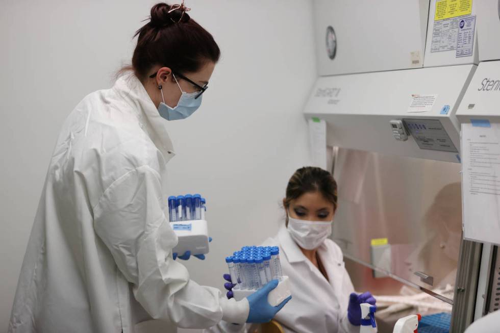 Lab manager Monika Karney, left, collects vials filled with viral transport medium from graduat ...