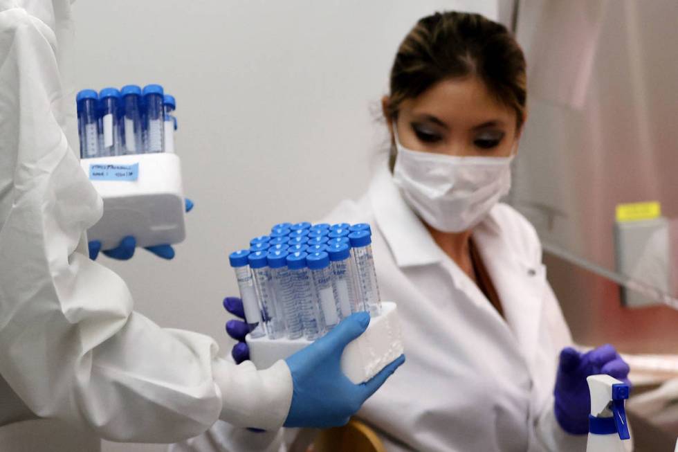 Lab manager Monika Karney, left, collects vials filled with viral transport medium from graduat ...