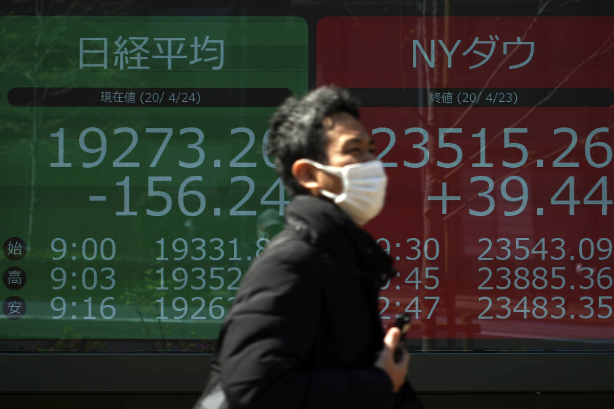 A man wearing a mask to help stop the spread of the new coronavirus walks past an electronic st ...