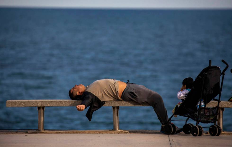 A man lies on a bench in front of the Mediterranean sea in Barcelona, Spain, Sunday, April 26, ...