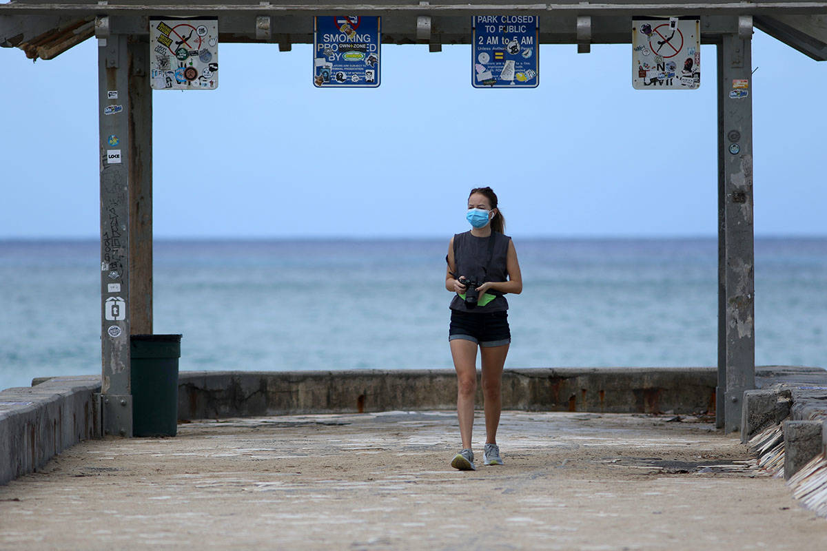 A woman wears a mask as she walks along a closed Waikiki Beach pier in Honolulu on Saturday, Ma ...