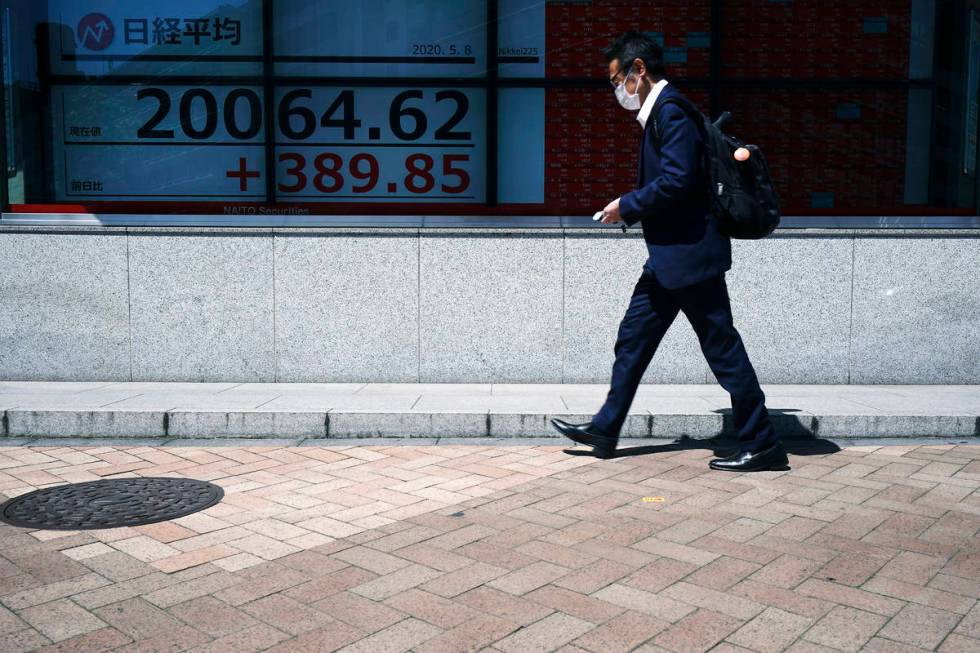 A man wearing a face mask to help curb the spread of the coronavirus walks past an electronic s ...