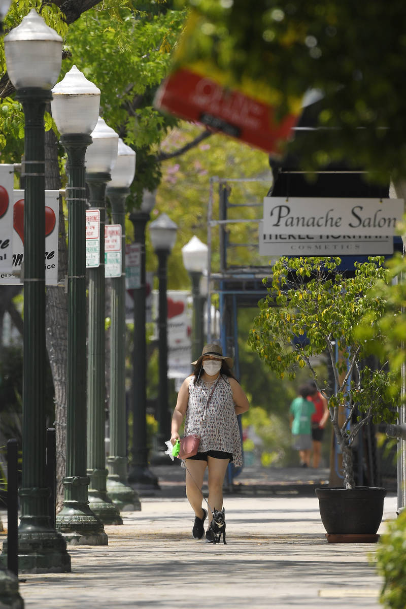 A woman walks her dog past shops during the coronavirus outbreak, Saturday, May 9, 2020, in Mon ...