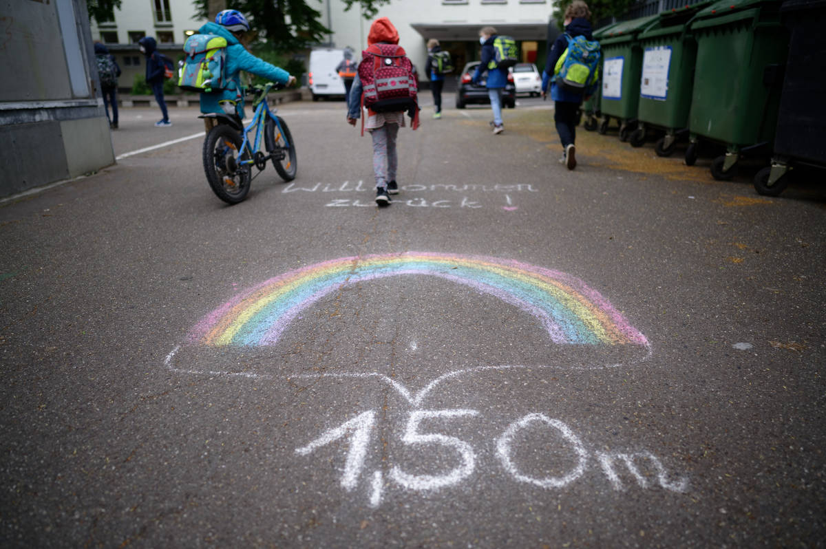 A writing on the ground remind students to keep distance as they arrive at a reopen primary sch ...