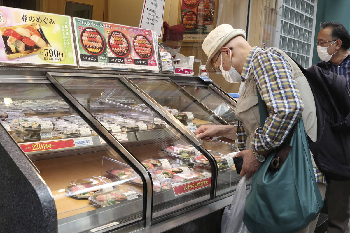 People wearing face masks to protect against the spread of the new coronavirus look at packs of ...