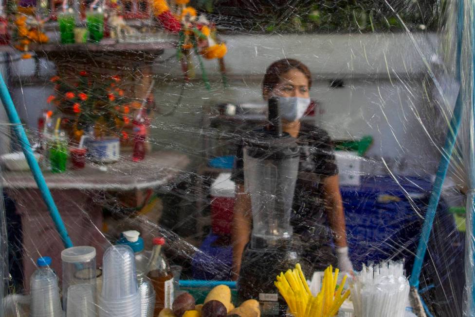 A street food seller stands behind a plastic devider sheet in Bangkok, Thailand, Wednesday, May ...