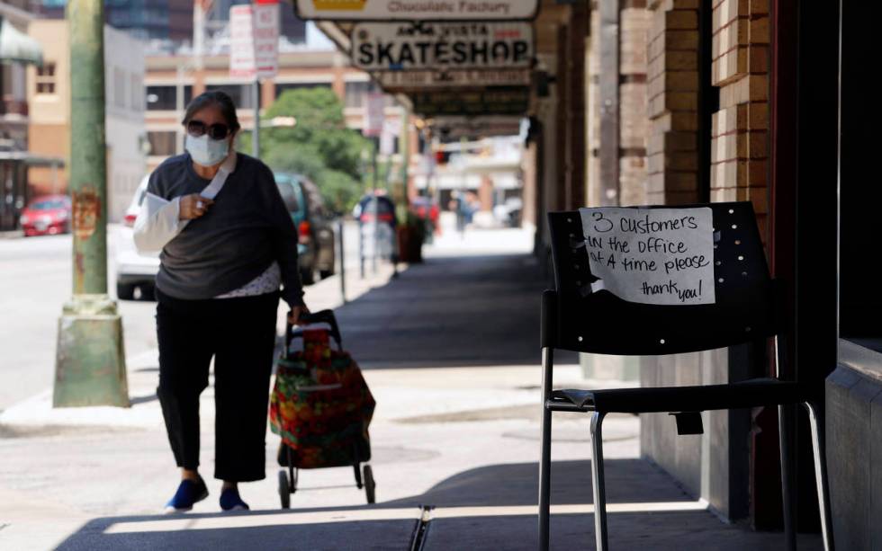 A woman wearing a face mask for protection against COVID-19 passes a business that has reopened ...