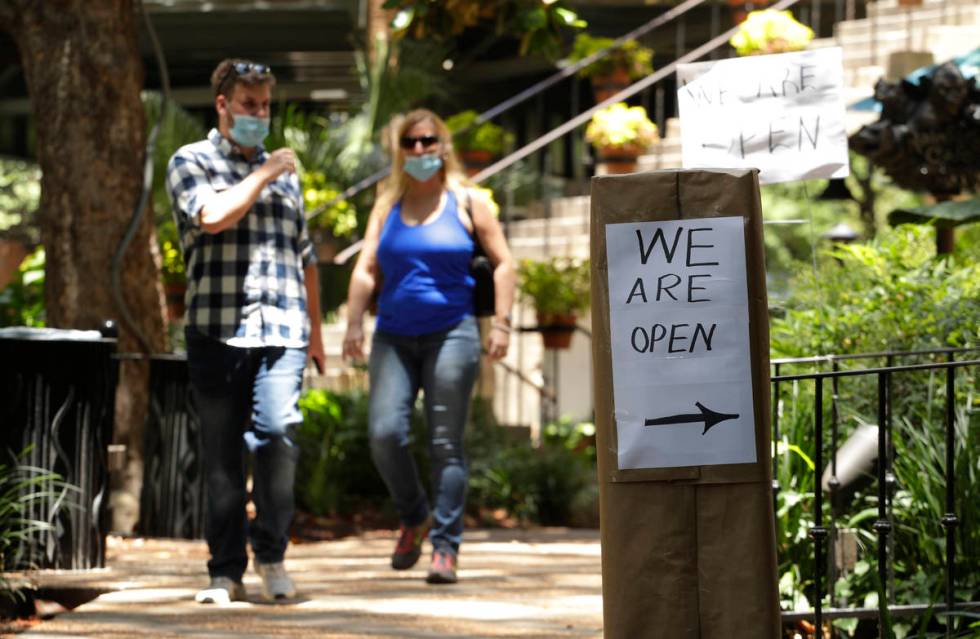 People wearing a face masks for protection against COVID-19 pass a business that has reopened i ...