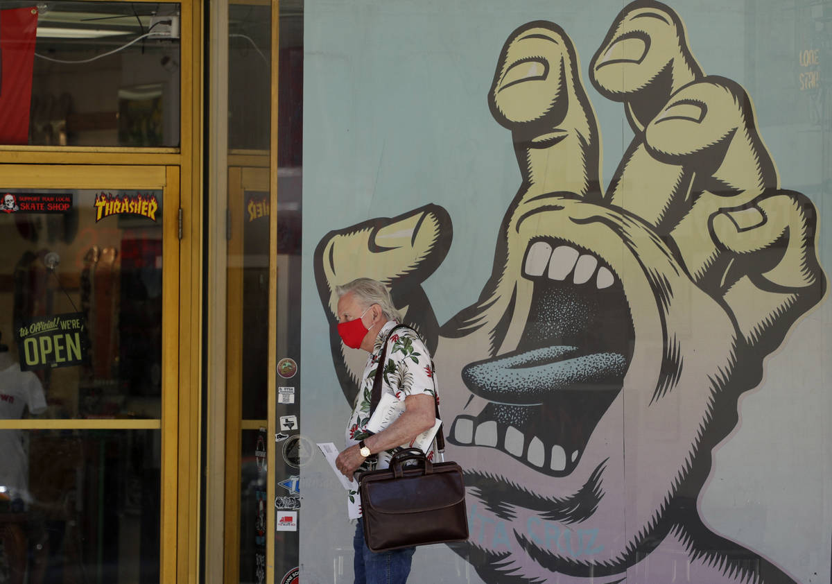 A man wearing a face mask for protection against COVID-19 passes a business that has reopened i ...