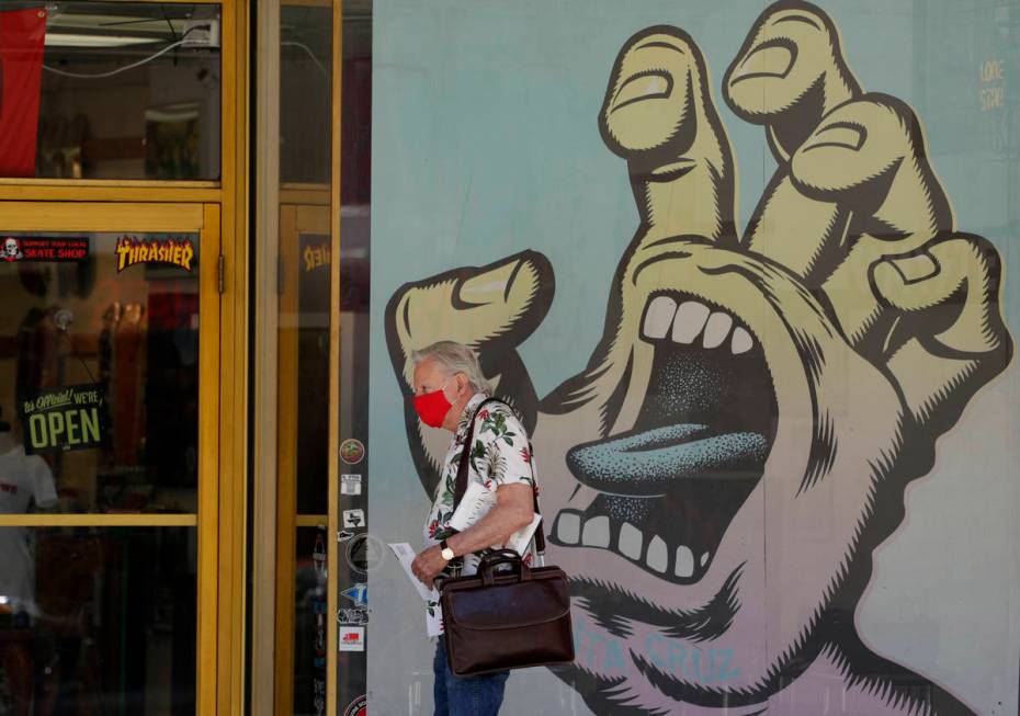 A man wearing a face mask for protection against COVID-19 passes a business that has reopened i ...