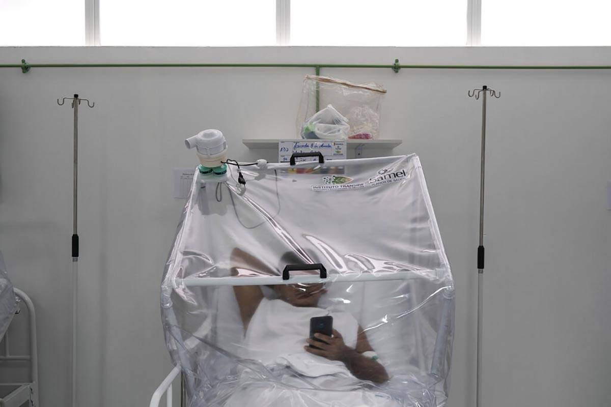 A COVID-19 patient uses his phone as he is treated inside a non-invasive ventilation system nam ...