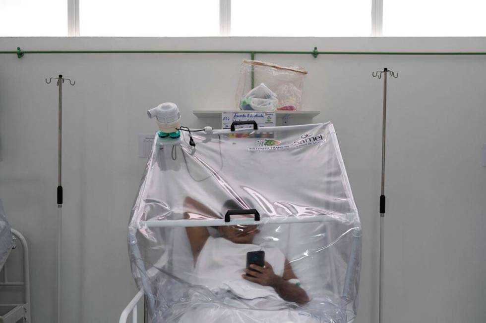 A COVID-19 patient uses his phone as he is treated inside a non-invasive ventilation system nam ...