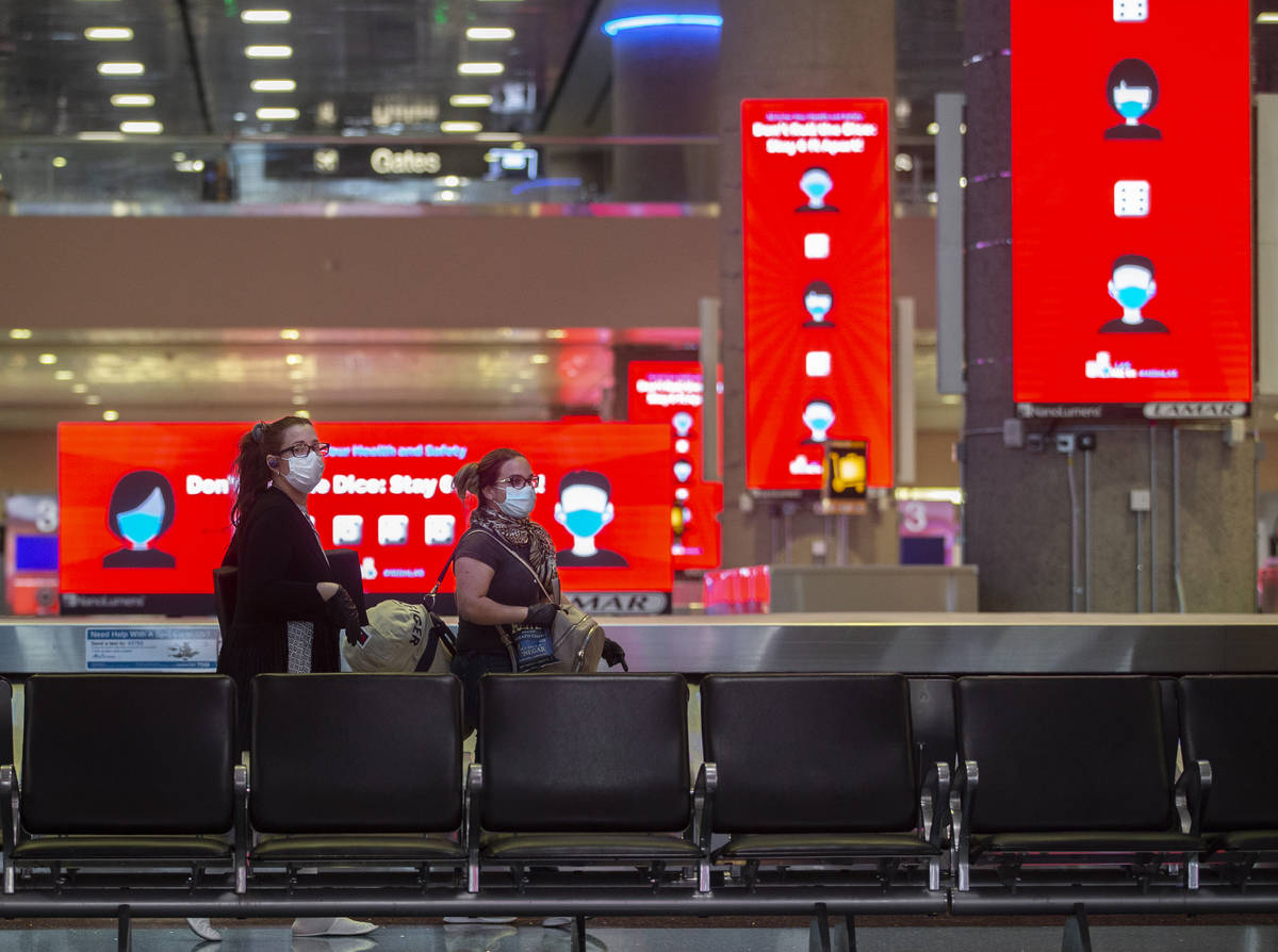 Travelers walk by new signage outlining coronavirus safety guidelines in the baggage claim area ...