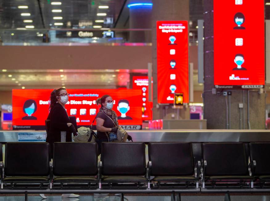 Travelers walk by new signage outlining coronavirus safety guidelines in the baggage claim area ...