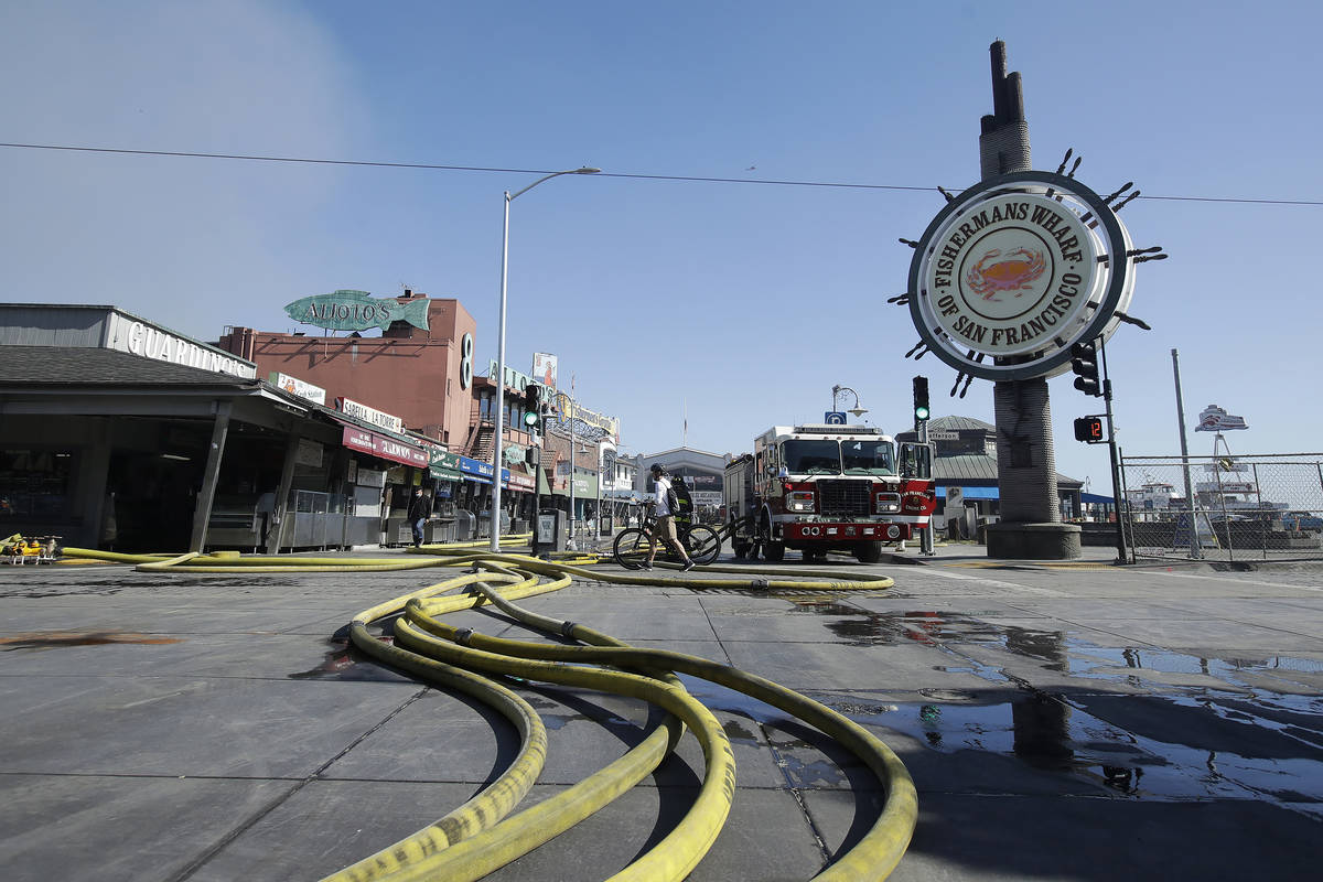 A runner passes over hoses after a fire broke out before dawn at Fisherman's Wharf in San Franc ...
