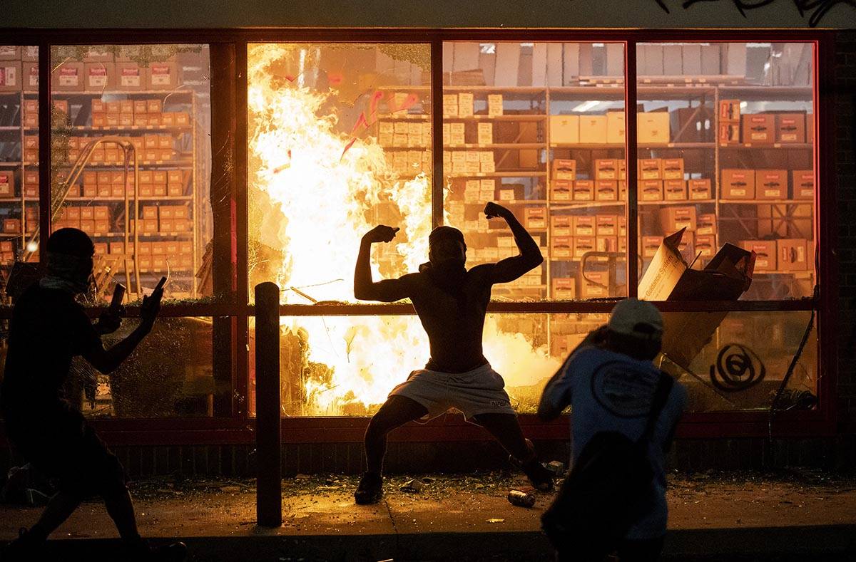 A man poses for photos in front of a fire at an AutoZone store, while protesters hold a rally f ...