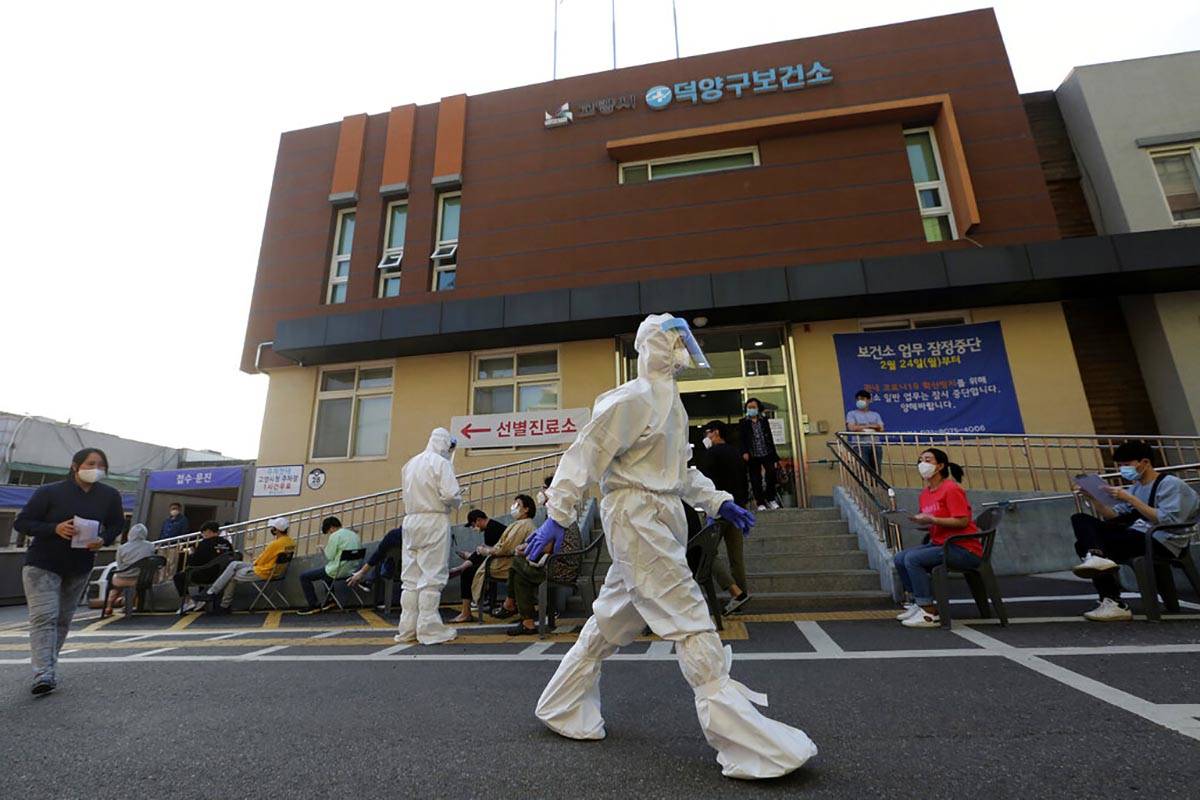 A health official wearing protective gear passes by people sitting and waiting for test for the ...