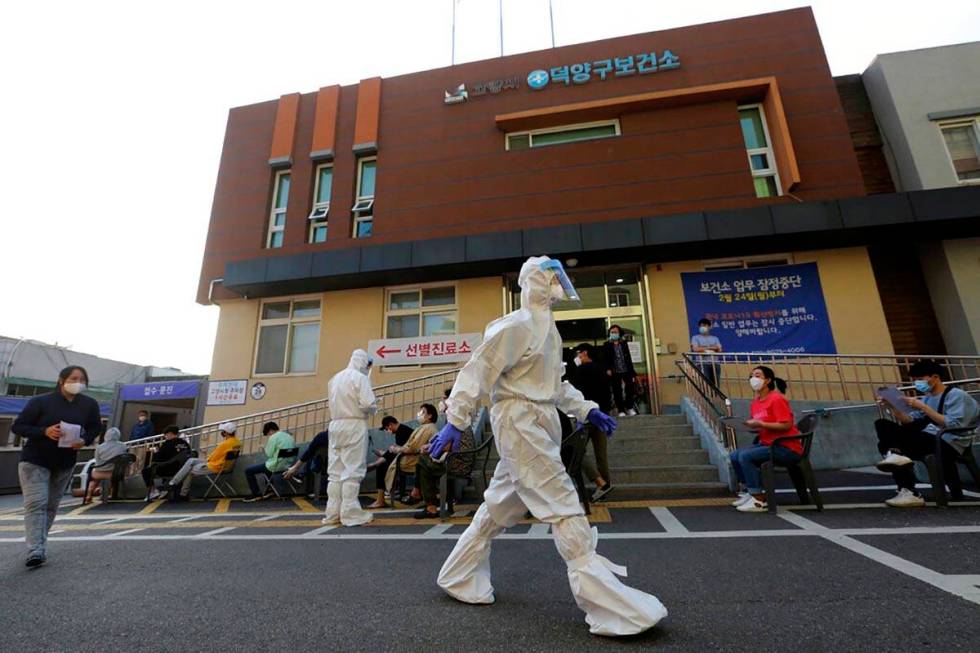 A health official wearing protective gear passes by people sitting and waiting for test for the ...