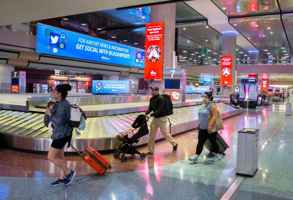 Travelers walk by new signage outlining coronavirus safety guidelines in the baggage claim area ...