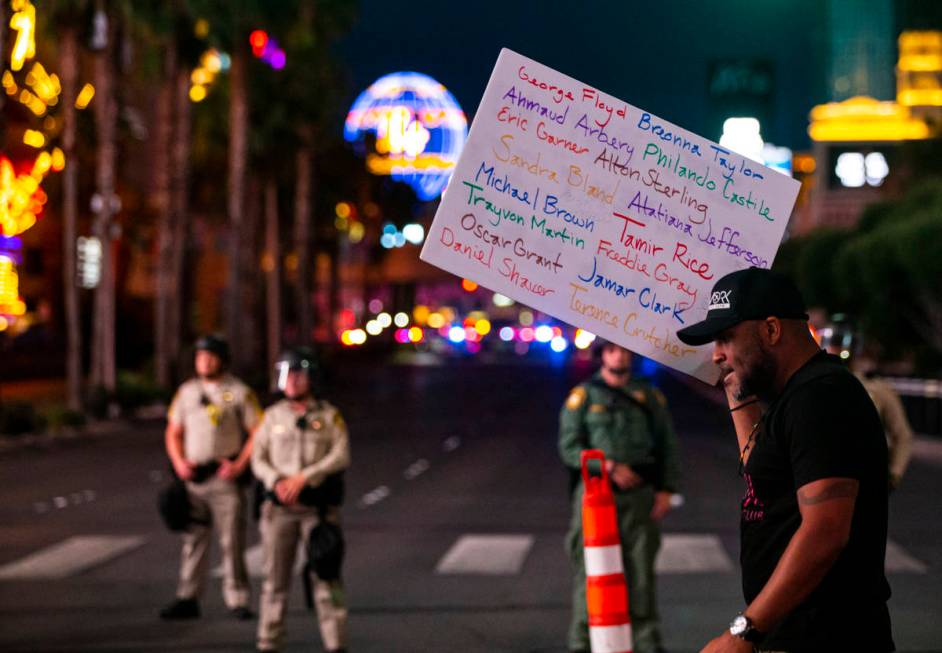 A man holds up a sign with the names of people of color killed by police as a police line block ...