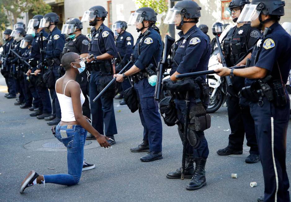 A masked protester kneels before San Jose police on Friday, May 29, 2020, in San Jose, Calif., ...