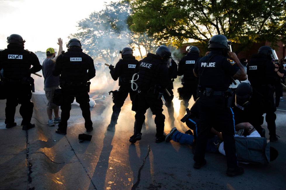 Police hold a man on the ground as tear gas is deployed and protesters rally near 72nd and Dodg ...