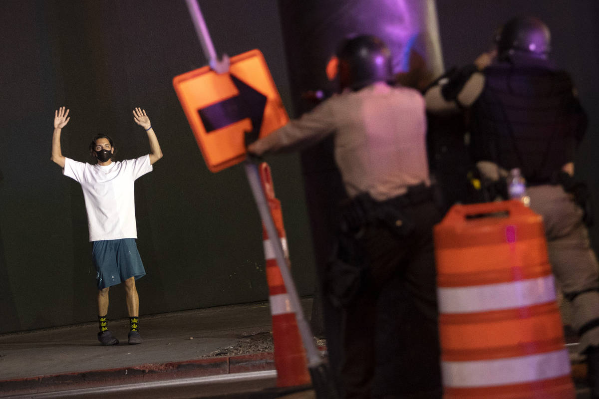 A protester puts his hands up while standing on the sidewalk as police officers ready to fire t ...