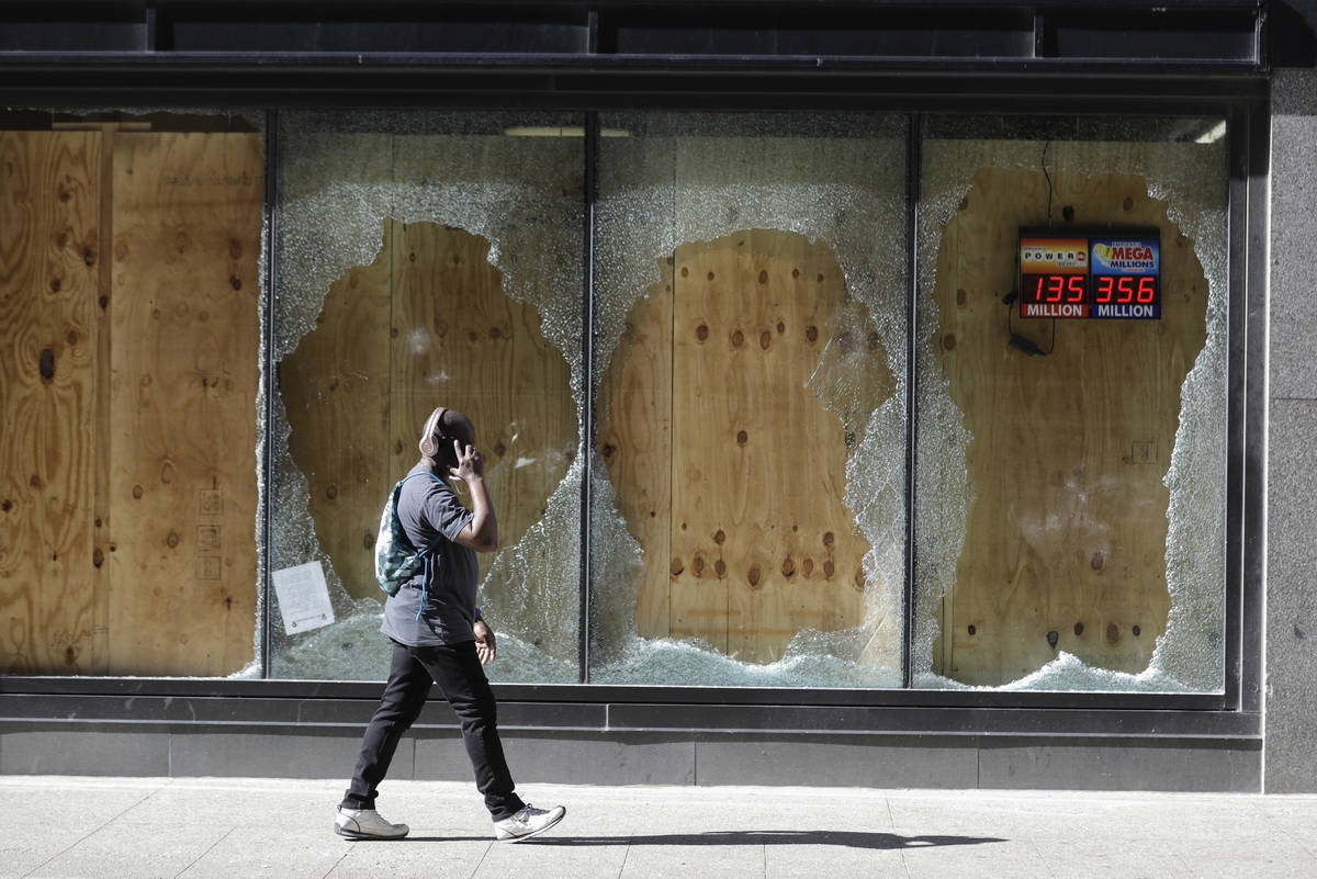 A man walks past broken and boarded up windows at a CVS store in downtown Louisville, Ky., Tues ...