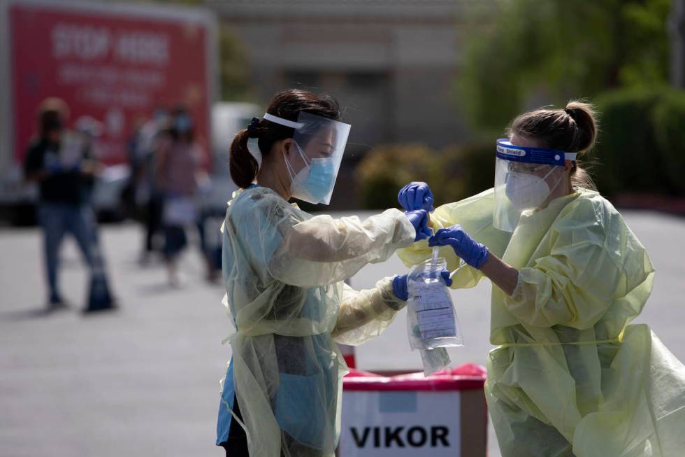 Volunteers place a nasal swab into a container at the COVID-19 drive-through testing site at Ca ...