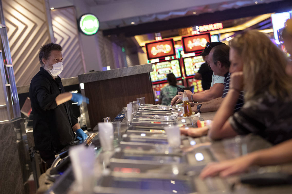 Bar seats are spaced out to keep social distance between people as a bartender wears a mask and ...