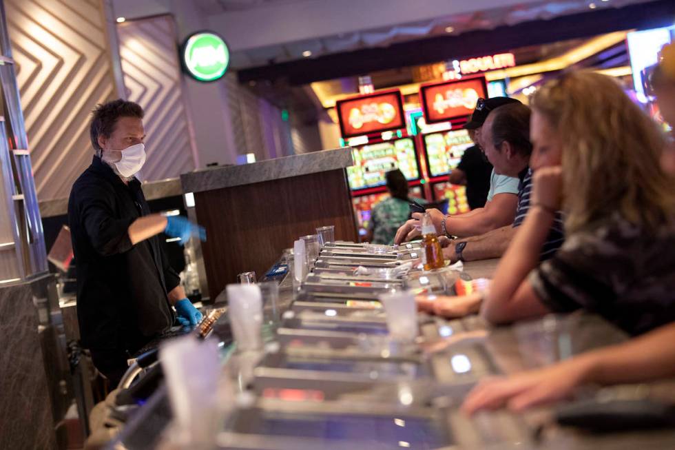 Bar seats are spaced out to keep social distance between people as a bartender wears a mask and ...