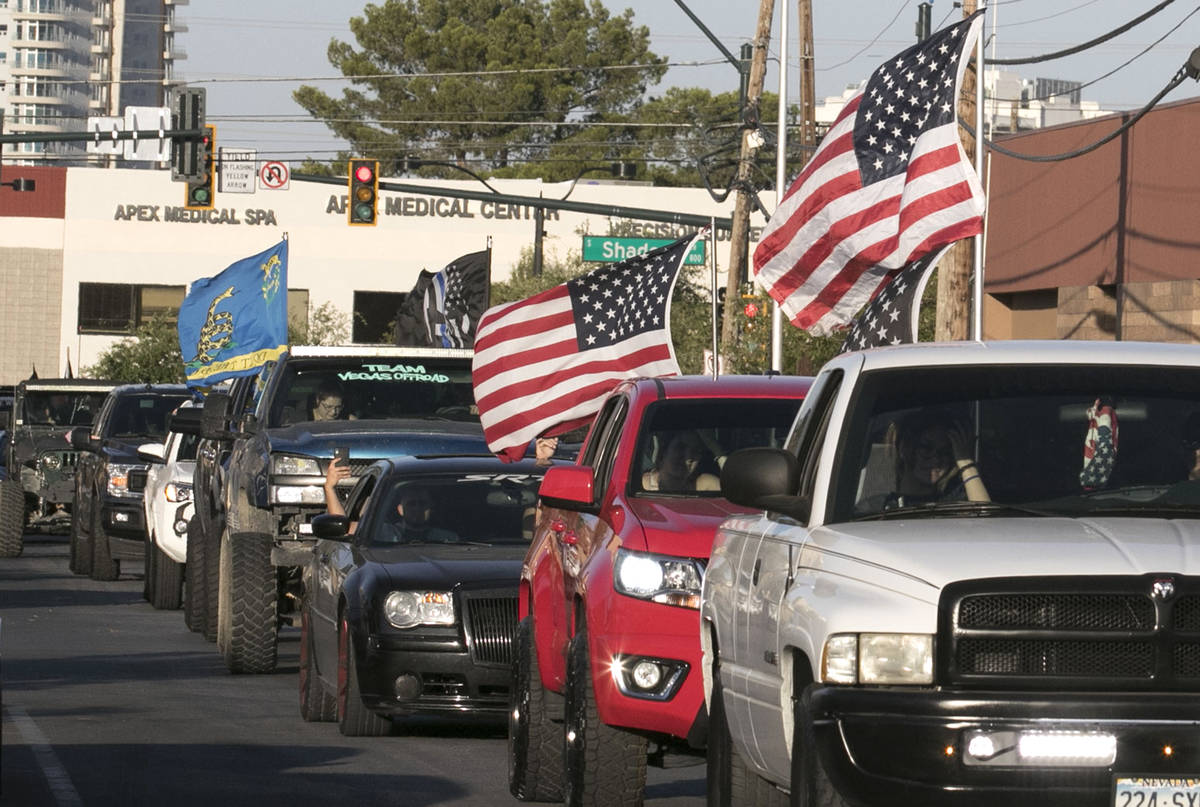 Drivers in pick up trucks and cars waving large American Flags drive past University Medical Ce ...