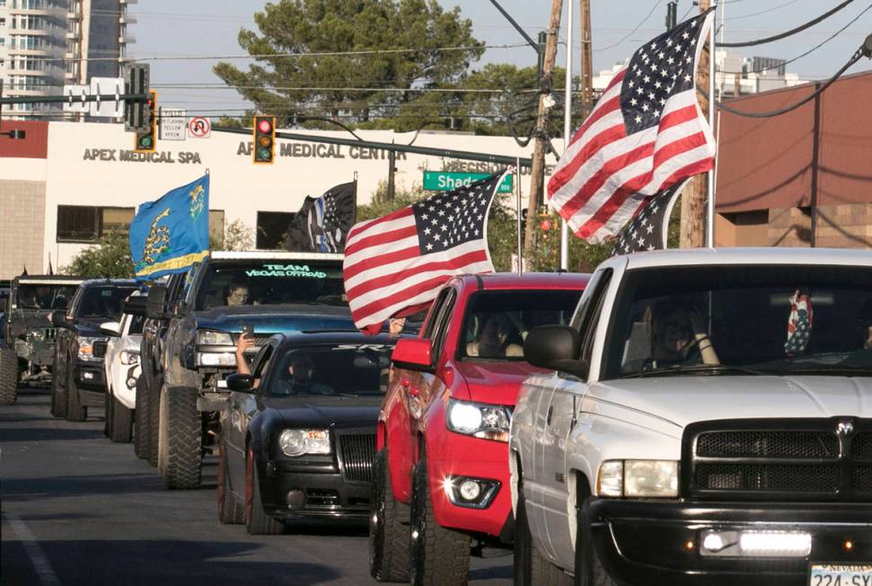 Drivers in pick up trucks and cars waving large American Flags drive past University Medical Ce ...