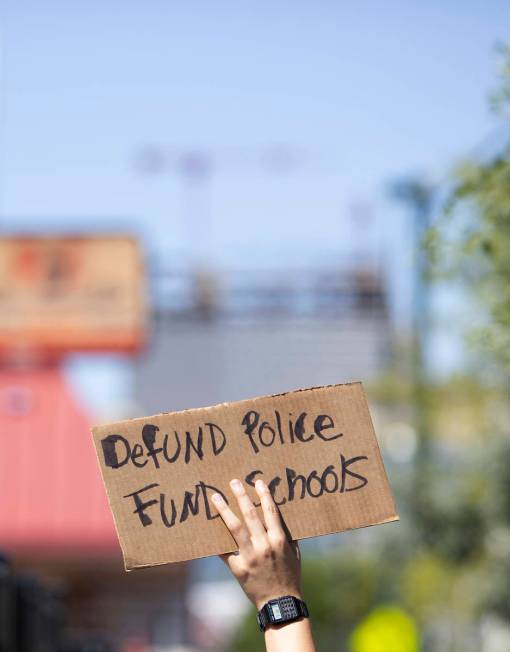 One marcher carries a sign calling for local politicians to defund police and fun schools on We ...