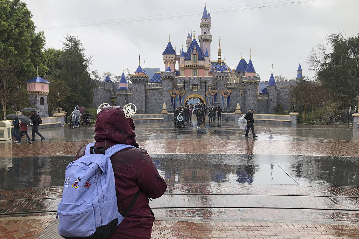 A visitor stands in the rain at Disneyland in Anaheim, Calif., Friday, March 13, 2020. Disneyla ...